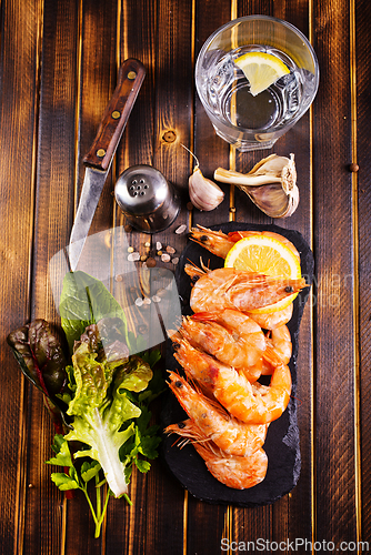 Image of Fried shrimps with garlic, lemon served on black plate on wooden table