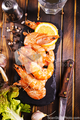Image of Fried shrimps with garlic, lemon served on black plate on wooden table