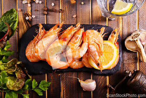 Image of Fried shrimps with garlic, lemon served on black plate on wooden table