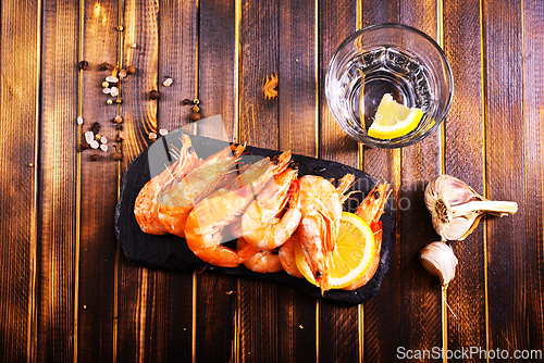 Image of Fried shrimps with garlic, lemon served on black plate on wooden table