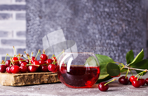 Image of Cherry juice in a glass and fresh cherries on a table