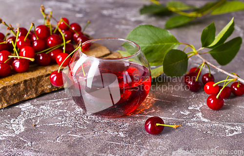 Image of Cherry juice in a glass and fresh cherries on a table