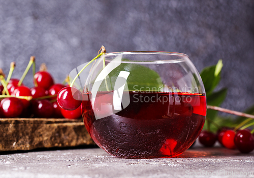 Image of Cherry juice in a glass and fresh cherries on a table