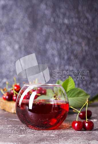 Image of Cherry juice in a glass and fresh cherries on a table