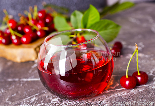 Image of Cherry juice in a glass and fresh cherries on a table