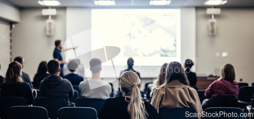 Image of Speaker giving a talk in conference hall at business event. Rear view of unrecognizable people in audience at the conference hall. Business and entrepreneurship concept.
