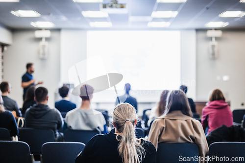 Image of Speaker giving a talk in conference hall at business event. Rear view of unrecognizable people in audience at the conference hall. Business and entrepreneurship concept.