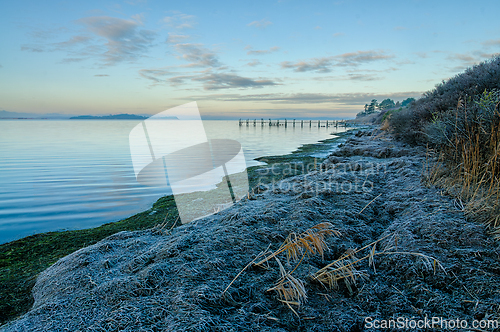 Image of Tranquil dawn at the water's edge with frost-kissed grass and a 