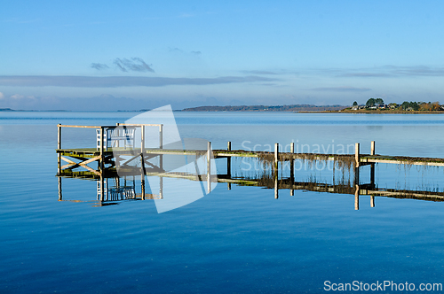 Image of Serene waters reflect a wooden dock under a clear sky at midday 