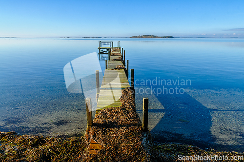 Image of Serene dock extends into calm waters under a clear blue sky at d