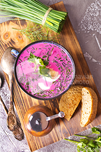 Image of A portion of beetroot soup with egg, dill, parsley and cucumber on a gray background.