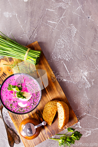 Image of A portion of beetroot soup with egg, dill, parsley and cucumber on a gray background.