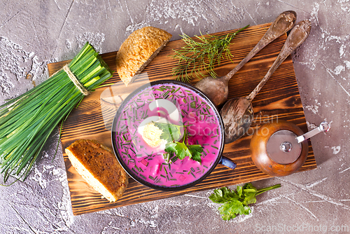 Image of A portion of beetroot soup with egg, dill, parsley and cucumber on a gray background.