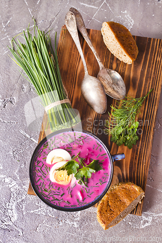 Image of A portion of beetroot soup with egg, dill, parsley and cucumber on a gray background.