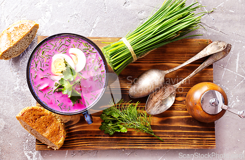 Image of A portion of beetroot soup with egg, dill, parsley and cucumber on a gray background.