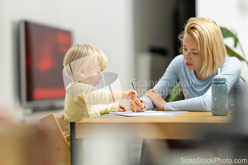 Image of Caring young Caucasian mother and small son drawing painting in notebook at home together. Loving mom or nanny having fun learning and playing with her little 1,5 year old infant baby boy child.