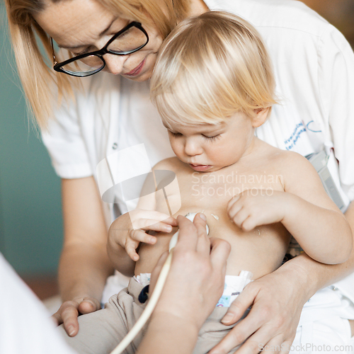 Image of Small child being checked for heart murmur by heart ultrasound exam by cardiologist as part of regular medical checkout at pediatrician.