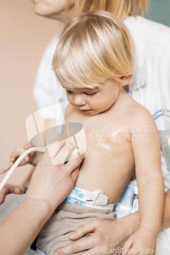Image of Small child being checked for heart murmur by heart ultrasound exam by cardiologist as part of regular medical checkout at pediatrician.