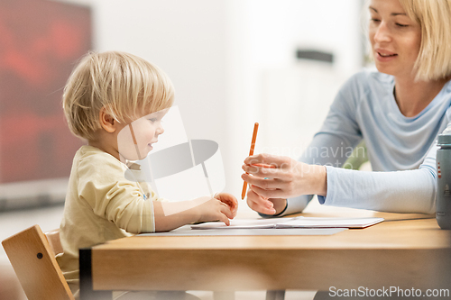 Image of Caring young Caucasian mother and small son drawing painting in notebook at home together. Loving mom or nanny having fun learning and playing with her little 1,5 year old infant baby boy child.