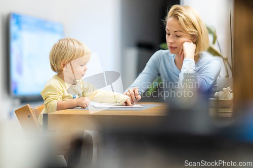 Image of Caring young Caucasian mother and small son drawing painting in notebook at home together. Loving mom or nanny having fun learning and playing with her little 1,5 year old infant baby boy child.
