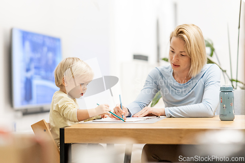 Image of Caring young Caucasian mother and small son drawing painting in notebook at home together. Loving mom or nanny having fun learning and playing with her little 1,5 year old infant baby boy child.