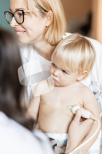 Image of Small child being checked for heart murmur by heart ultrasound exam by cardiologist as part of regular medical checkout at pediatrician.
