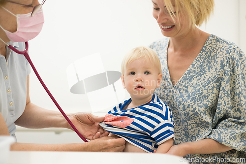 Image of Infant baby boy child being examined by his pediatrician doctor during a standard medical checkup in presence and comfort of his mother. National public health and childs care care koncept.