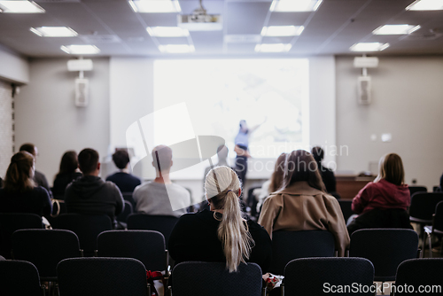 Image of Speaker giving a talk in conference hall at business event. Rear view of unrecognizable people in audience at the conference hall. Business and entrepreneurship concept.