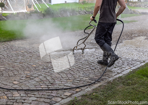 Image of Professional cleaning service worker power washing cobblestone