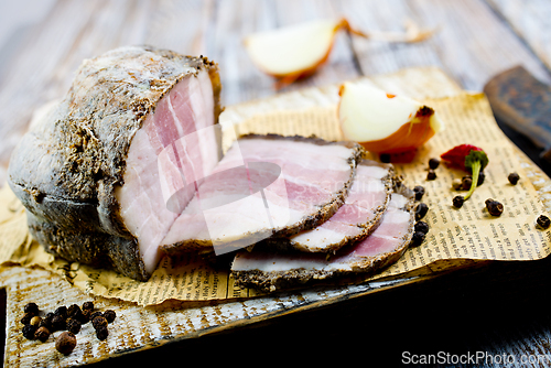 Image of Smoked lard, bacon, half a piece, on a wooden dark craft board. Top view, close-up.