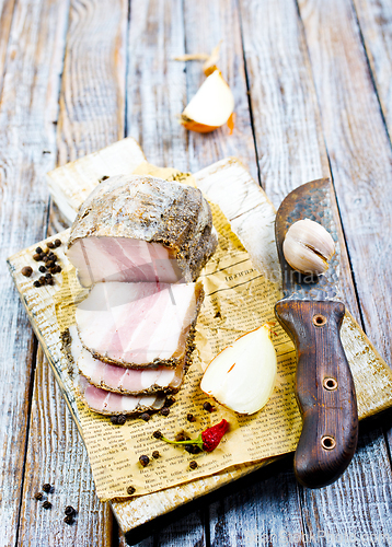 Image of Smoked lard, bacon, half a piece, on a wooden dark craft board. Top view, close-up.