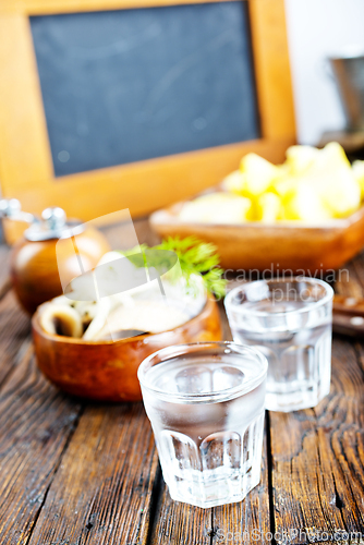 Image of one empty second vodka-filled glass surrounded by a snack with herring and onions