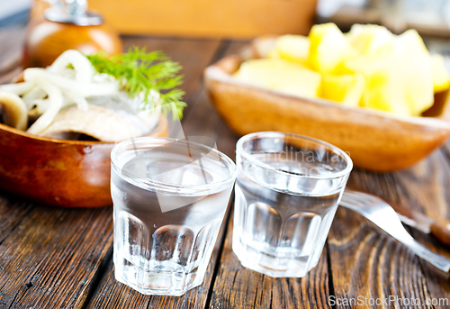 Image of one empty second vodka-filled glass surrounded by a snack with herring and onions