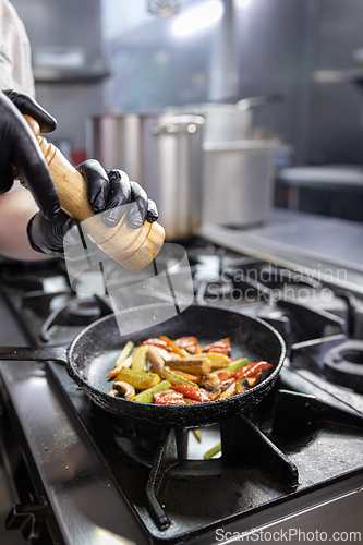 Image of Chef grinding spices into a pan of grilled vegetables