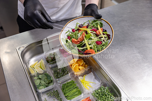 Image of Chef using tongs and holding plate with fresh salad