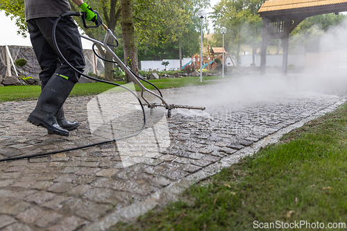 Image of Professional cleaning service worker power washing cobblestone