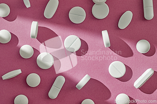 Image of white pills on sunny pink background