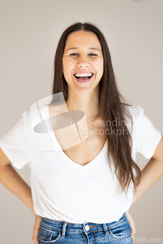 Image of Portrait of confident beautiful woman with long brown hair, wearing casual clothes, standing in relaxed pose with hands in pockets, smiling with white teeth at camera, studio background.