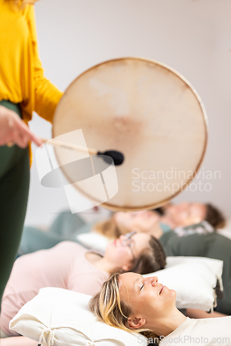 Image of Group therapy session with Tibetan drum for group of women lying on wooden floor surrounded by copper bowls. Meditation and relaxation