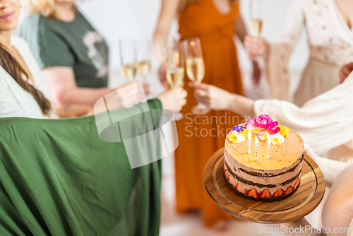 Image of Birthday surprise party. Group of cheerful female friends celebrating personal success stories. Smiling girls toasting with glasses of champagne one holding a birthday cake with candles to blow
