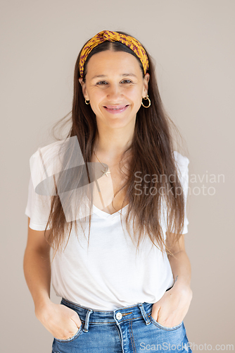 Image of Portrait of confident beautiful woman with long brown hair, wearing casual clothes, standing in relaxed pose with hands in pockets, smiling with white teeth at camera, studio background.