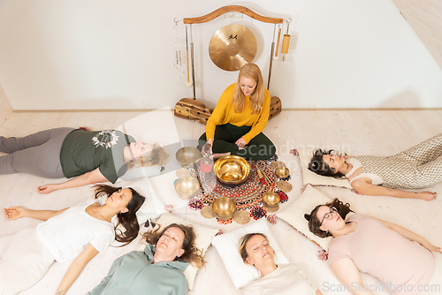 Image of Group therapy session with Tibetan singing bowls for group of women lying on wooden floor surrounded by copper bowls. Meditation and relaxation