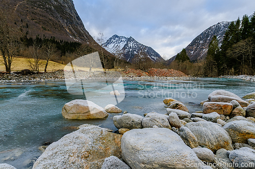 Image of Majestic mountains frame a serene river as winter slowly melts i
