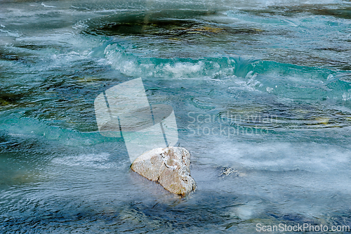 Image of Clear water flows around a solitary rock in a tranquil river set
