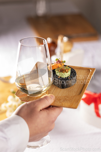 Image of Waiter serving a glass of white wine and black bread canapes