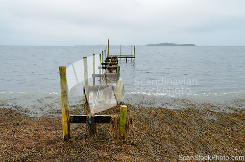 Image of Weathered dock extends into calm waters along the shoreline in a