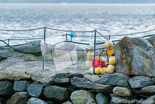 Image of Buoys and chains resting on rocky pier beside calm water in earl
