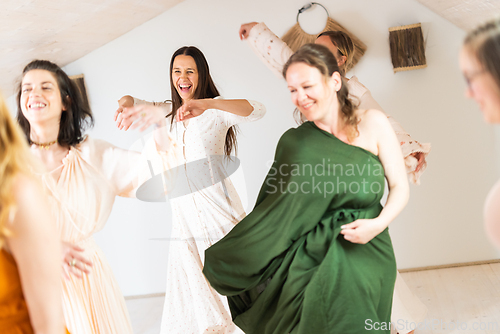 Image of Group of cheerful women all ages, happy people dancing together wearing traditional colorful dresses and hippy clothes. Free people enjoying leisure activity, emphasizing friendship, fun, movement.
