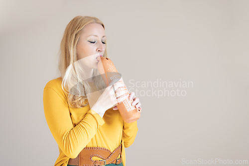 Image of Portrait of female musician playing on traditional clay flute. Woman playing ocarina.