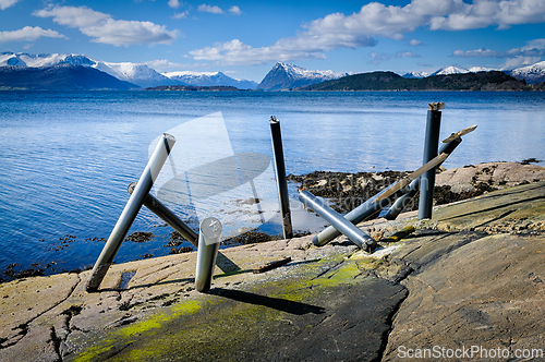 Image of Metal poles emerge from the rocky shore against a stunning coast